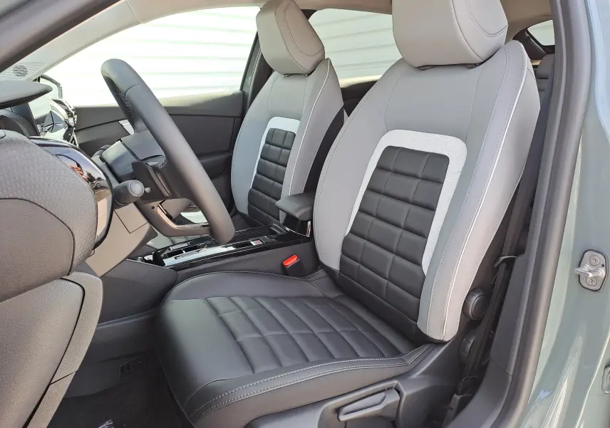 Vue intérieure côté conducteur de la Citroën C4 hybride 2025 avec sièges bicolores gris clair et noir, volant et console centrale visibles.