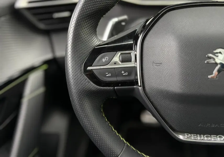 Gros plan sur le volant cuir noir perforé avec surpiqûres vertes et logo Peugeot au centre du Peugeot 208 GT.