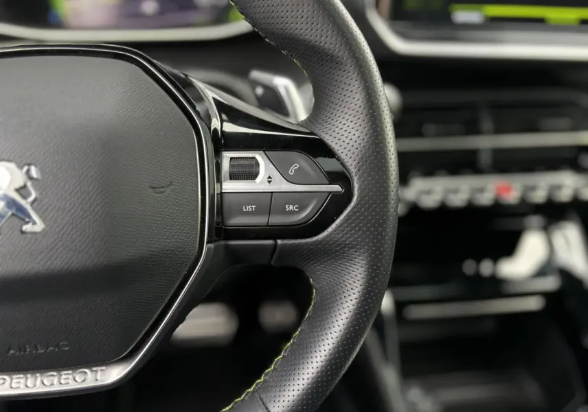 Gros plan sur le volant cuir noir perforé avec surpiqûres vertes et commandes multimédia de la Peugeot 208 GT 2023.