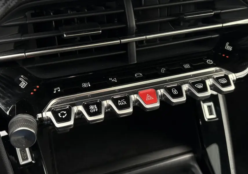 Gros plan sur la console centrale noire brillante de la Peugeot 208 GT avec ses boutons métalliques et touches tactiles rétroéclairées
