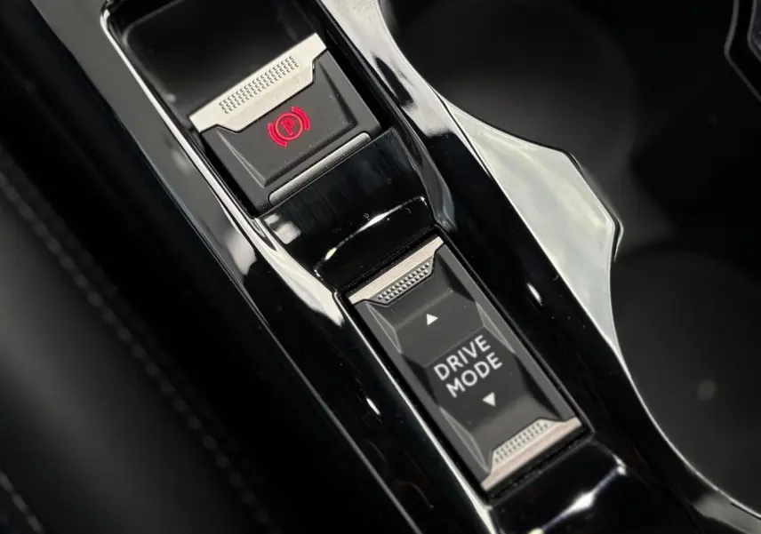 Gros plan sur la console centrale noire brillante du Peugeot 208 GT 2023 avec bouton frein à main électrique et sélection mode de conduite.
