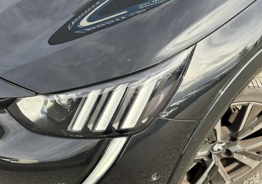 Gros plan sur le phare avant gauche et la jante alliage 17'' noir perla de la Peugeot 208 GT 2023.