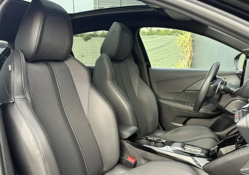Vue intérieure côté droit de la Peugeot 208 GT 2023 avec sièges sport noirs et toit panoramique ouvert.
