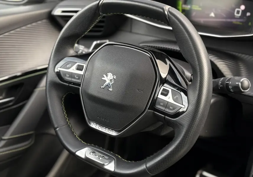 Volant cuir noir avec surpiqûres vertes et badge GT de la Peugeot 208 1.2 PureTech 130 vue de face intérieure.