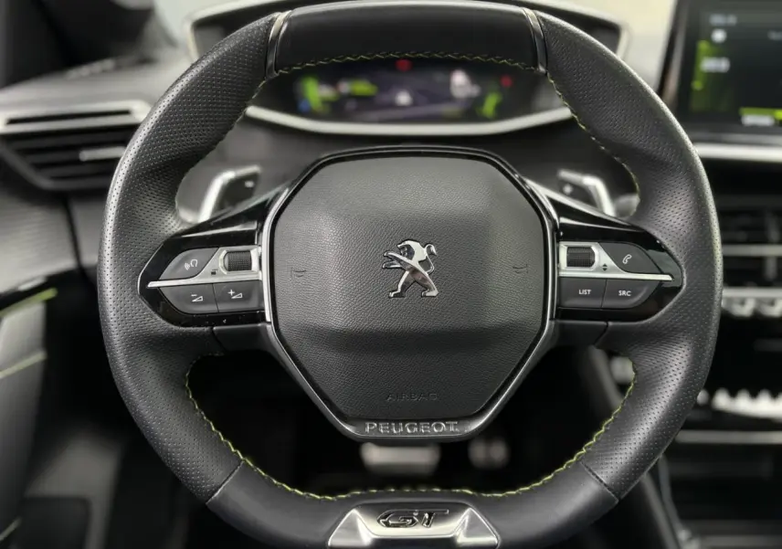 Gros plan sur le volant cuir noir avec surpiqûres vertes et logo Peugeot GT du tableau de bord de la 208 Noir Perla.