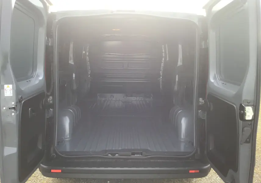 Vue arrière du Renault Trafic Fourgon gris urbain 2025 avec portes ouvertes montrant l’espace de chargement vide.
