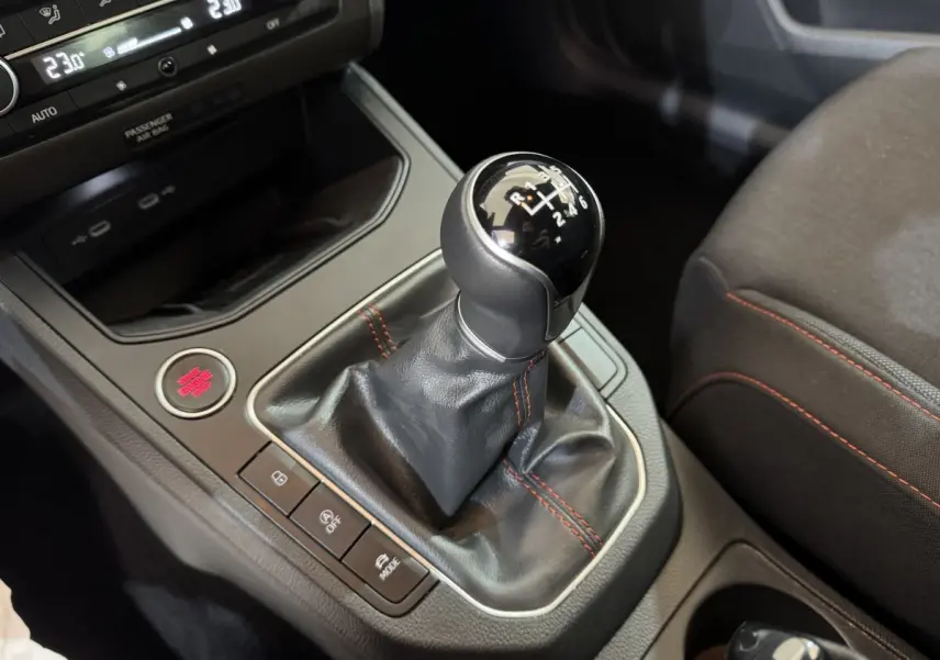 Gros plan sur le levier de vitesses manuel noir avec surpiqûres rouges dans l'habitacle de la SEAT Ibiza rouge 2024.