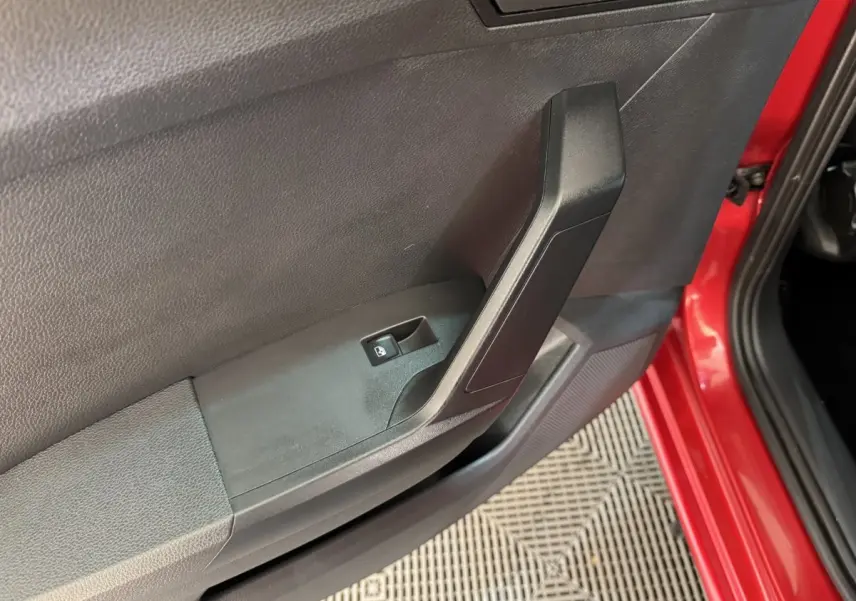 Gros plan sur la poignée intérieure et le bouton de verrouillage de la porte côté gauche d'une SEAT Ibiza rouge 2024.
