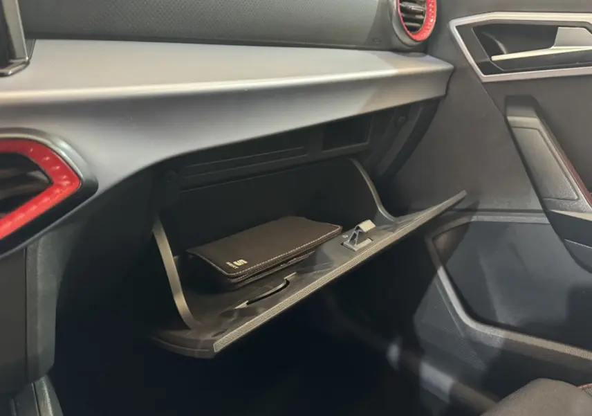 Gros plan sur la boîte à gants ouverte côté passager d'une SEAT IBIZA 1.0 TSI 110 FR 2024 avec surpiqûres rouges.