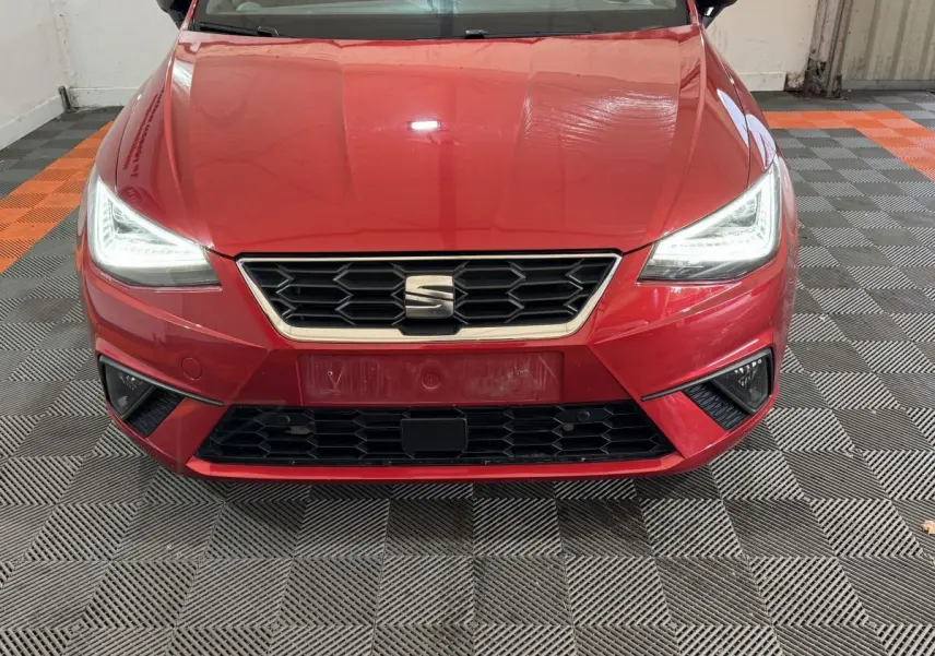 Vue frontale d'une SEAT IBIZA 1.0 TSI 110 FR rouge avec phares LED allumés et calandre hexagonale noire.