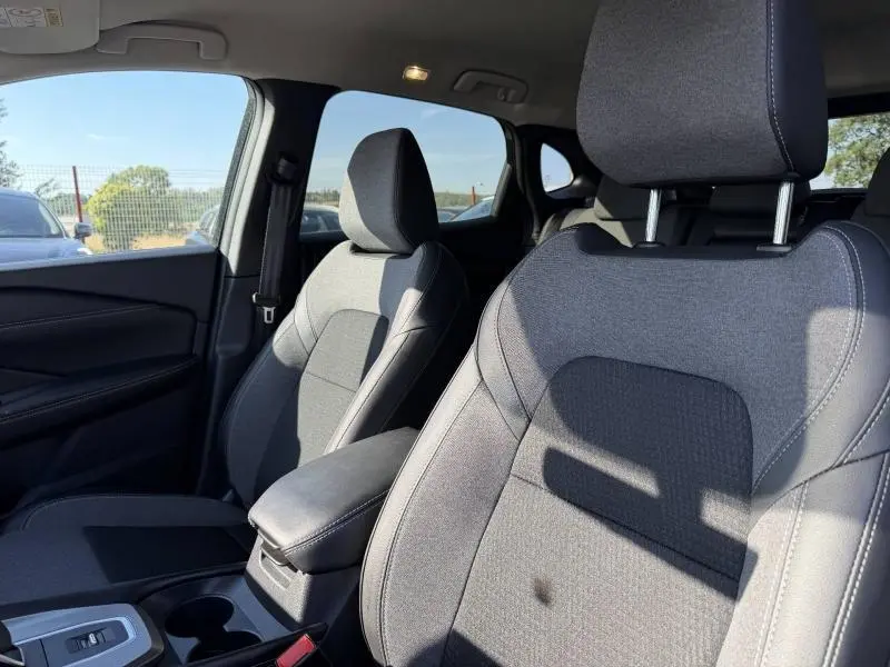 Vue intérieure rapprochée des sièges avant gris du Nissan Qashqai 2025 avec accoudoir central et porte-gobelets.