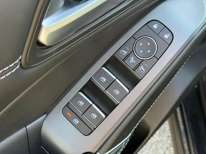 Gros plan sur les commandes des vitres et rétroviseurs côté conducteur en noir avec surpiqûres blanches dans un Nissan Qashqai 2025.