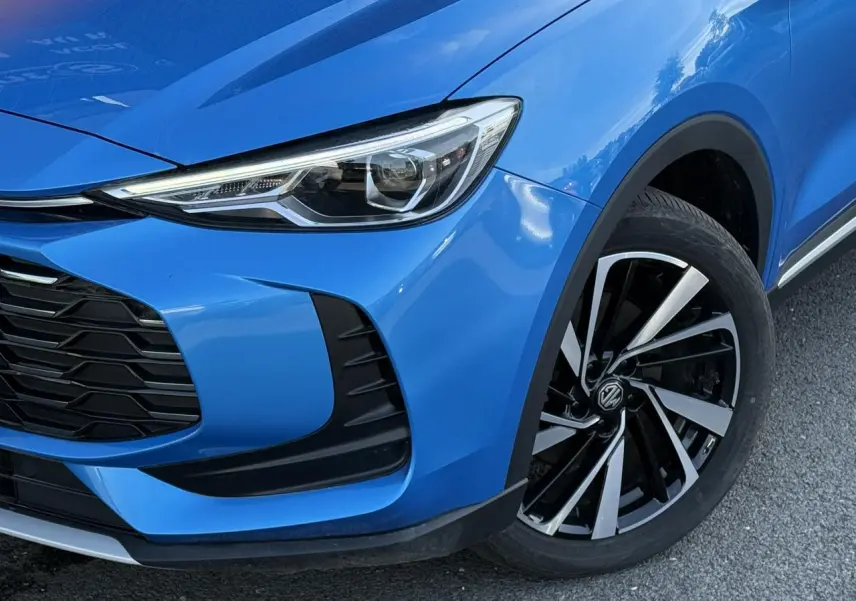 Gros plan sur l'avant droit bleu Como du MG ZS 1.5 Hybrid+ 197 Luxury, mettant en valeur le phare LED et la jante alliage 18 pouces.
