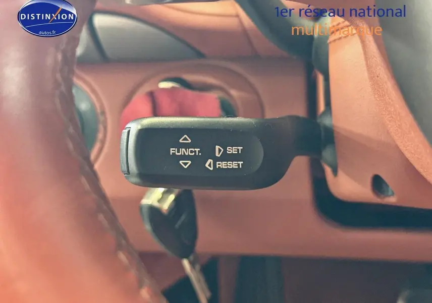 Gros plan sur la commande de régulateur de vitesse dans l'habitacle cuir marron d'une Porsche 911 gris 2009.