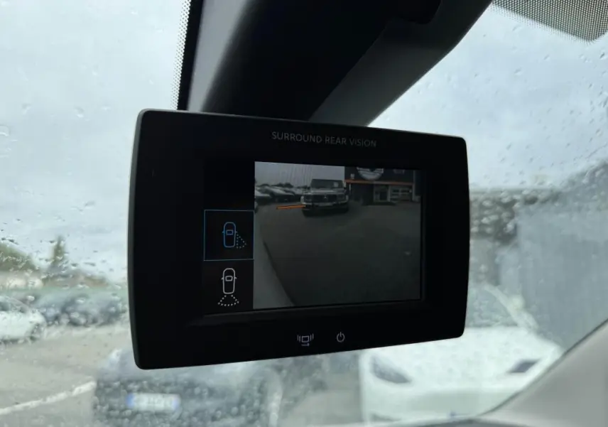 Écran de caméra de recul du Citroën Berlingo blanc montrant l'arrière et un véhicule garé en extérieur sous la pluie.