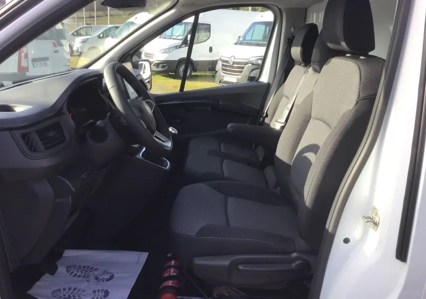 Vue intérieure côté conducteur du Renault Trafic blanc, montrant les sièges avant et le tableau de bord avec volant.