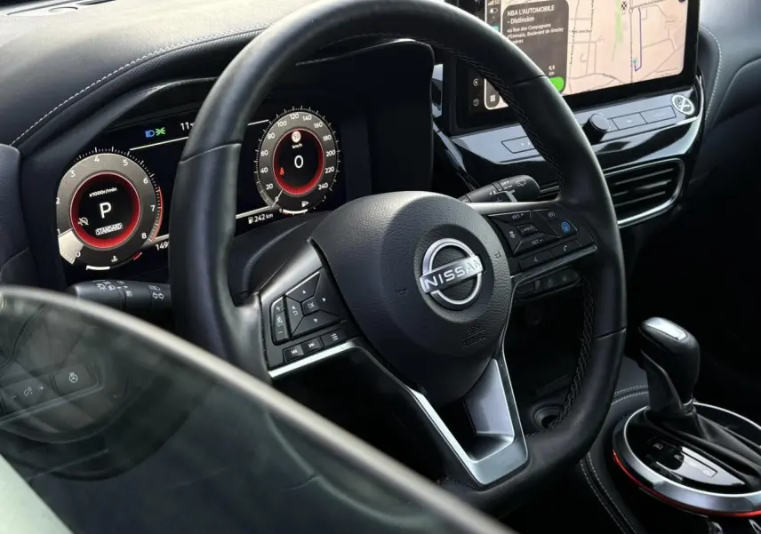 Vue intérieure centrée sur le volant Nissan et le combiné digital, avec écran tactile et levier de vitesse noir.