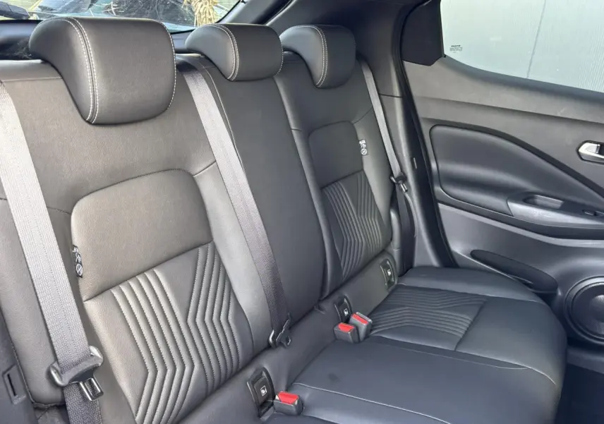 Vue intérieure arrière du Nissan Juke 2024, sièges noirs en cuir avec surpiqûres et ceintures grises visibles.