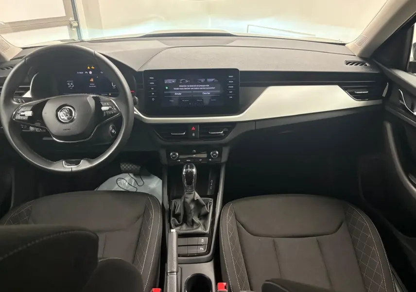 Intérieur du Skoda Kamiq 2023 vu de face, tableau de bord moderne avec écran tactile et sièges noirs à surpiqûres grises.