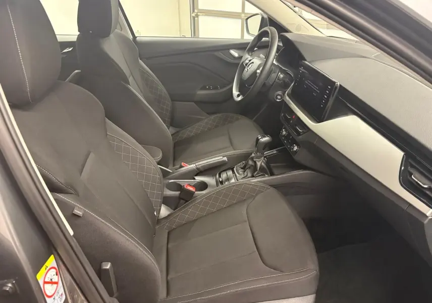 Intérieur avant droit du Skoda Kamiq 2023 gris graphite, sièges tissu noir avec surpiqûres et tableau de bord moderne.