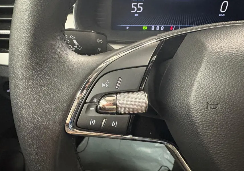 Gros plan sur les commandes gauche du volant du Skoda Kamiq 2023 gris graphite, avec affichage numérique en arrière-plan.