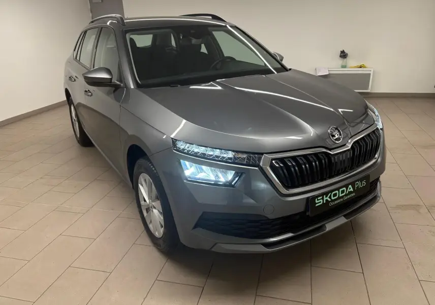 Vue 3/4 avant droite d'un Skoda Kamiq gris graphite avec phares allumés dans un intérieur neutre.