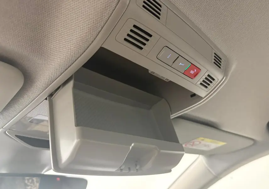 Vue intérieure en plongée du compartiment de rangement ouvert au plafond du Skoda Kamiq 2023 gris graphite, avec commandes SOS visibles.