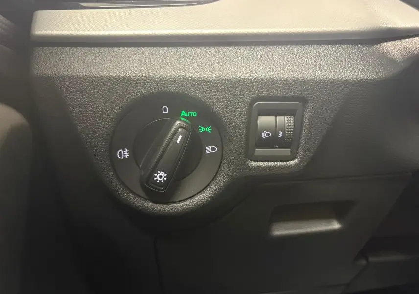 Gros plan sur la commande des phares avec réglage automatique dans l’habitacle du Skoda Kamiq gris graphite 2023.