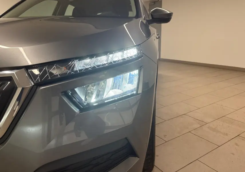 Gros plan sur l'avant droit du Skoda Kamiq 2023 gris graphite, mettant en valeur ses phares LED allumés et la calandre.