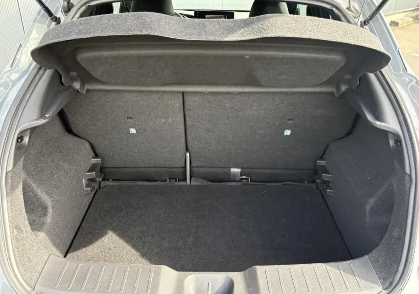 Coffre ouvert du Nissan Juke gris Ceramic 2025, vue arrière montrant le plancher de coffre modulable et l'espace de rangement.