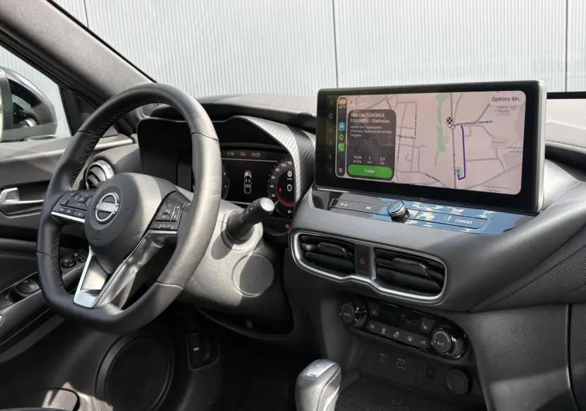 Vue intérieure côté conducteur du Nissan Juke 2025, tableau de bord noir avec écran tactile GPS et volant multifonction.
