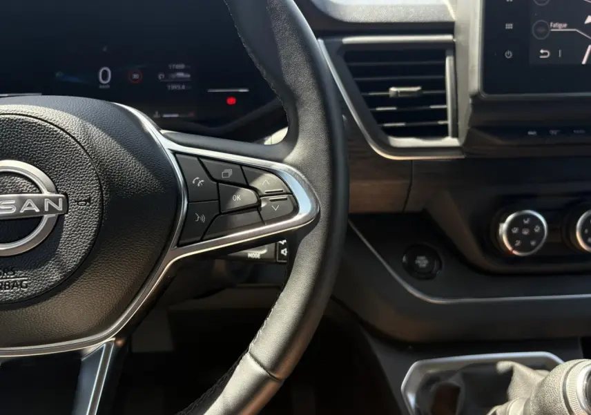 Vue rapprochée du volant et tableau de bord du Nissan Primastar Combi noir, avec commandes au volant et écran tactile visible.