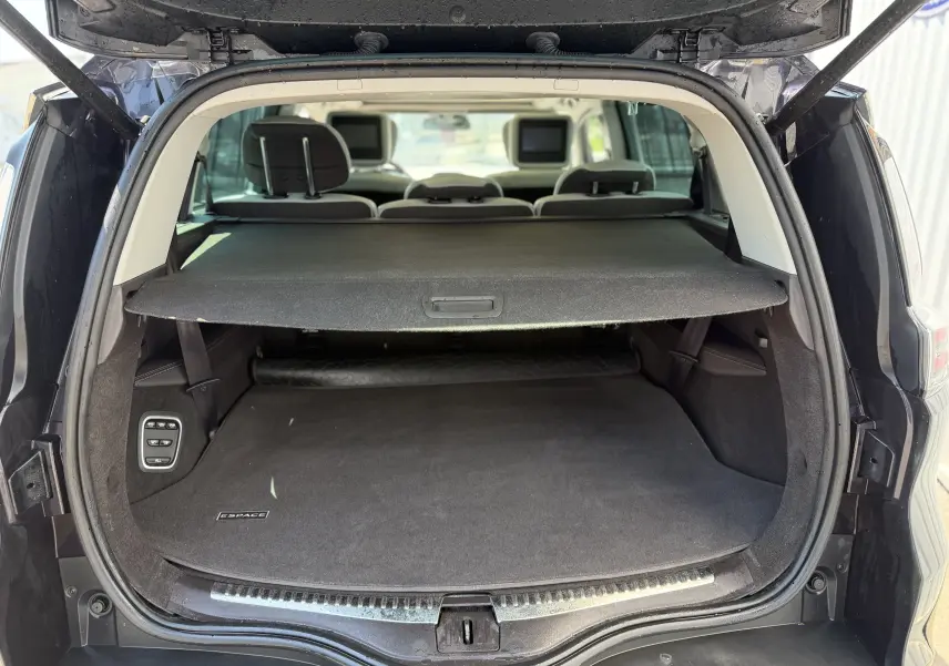 Vue arrière du coffre ouvert du Renault Espace V noir, avec cache-bagages déployé et sièges arrière équipés d'écrans intégrés.