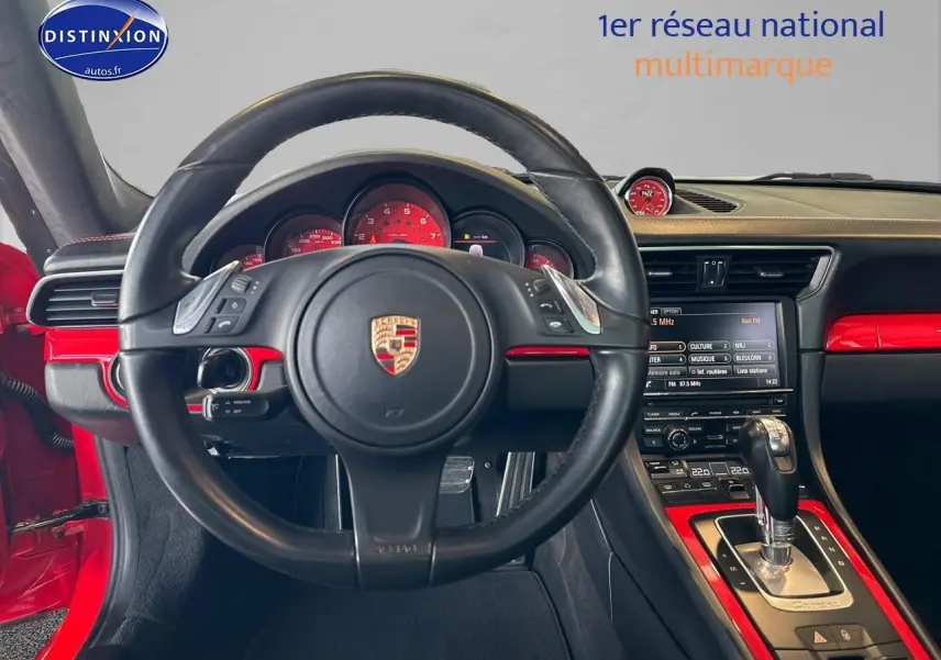 Vue intérieure centrée sur le volant cuir noir et le tableau de bord rouge de la Porsche 911 Carrera 4 PDK rouge.