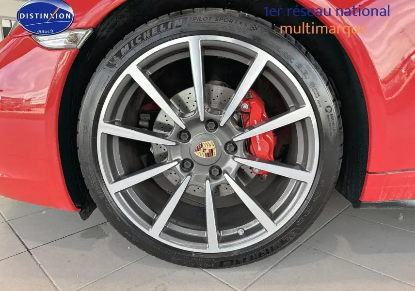 Gros plan sur la jante alu grise et l'étrier de frein rouge d'une Porsche 911 Carrera 4 rouge côté avant droit.