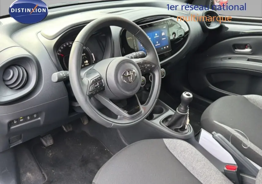 Vue intérieure de face du poste de conduite noir de la Toyota Aygo X 2025 avec volant multifonction et boîte manuelle.
