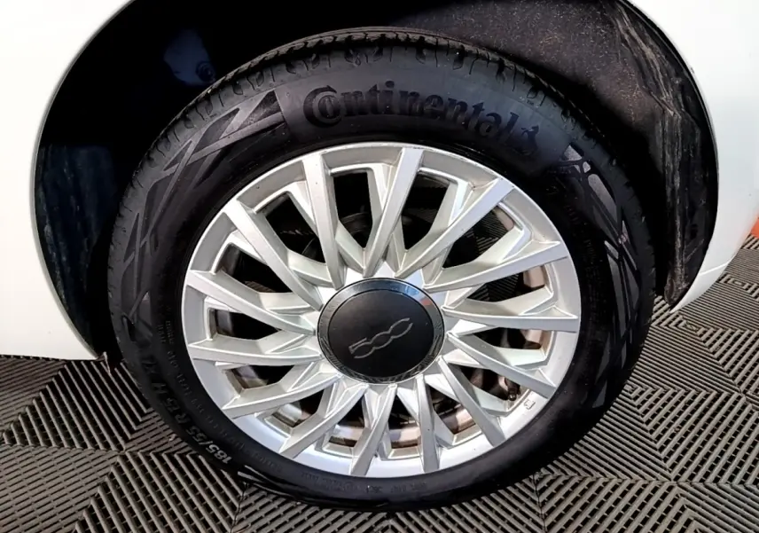 Gros plan sur la roue avant droite d'une FIAT 500 blanche, avec jante argentée au design étoilé et pneu Continental.