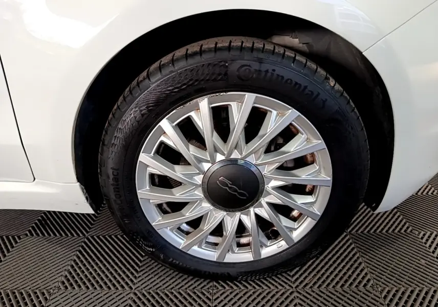 Gros plan sur la roue avant droite blanche d'une FIAT 500 Dolcevita avec jante argentée à motifs rayonnants.