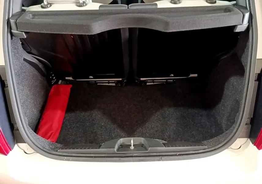 Coffre ouvert vu de l'arrière d'une Fiat 500 blanche avec intérieur noir et sac rouge sur le côté gauche.