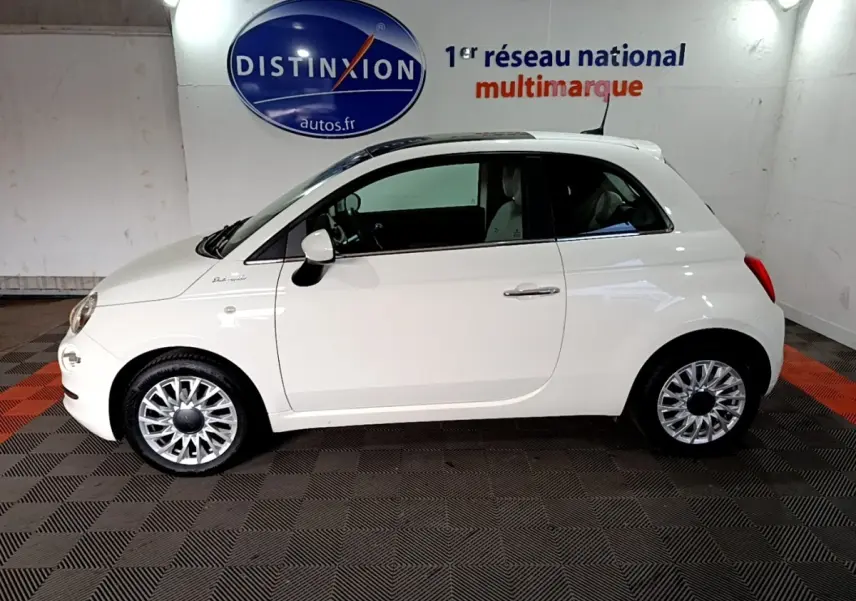 Profil côté gauche d'une Fiat 500 blanche Hybrid 2021, avec jantes argentées et toit blanc dans un showroom.