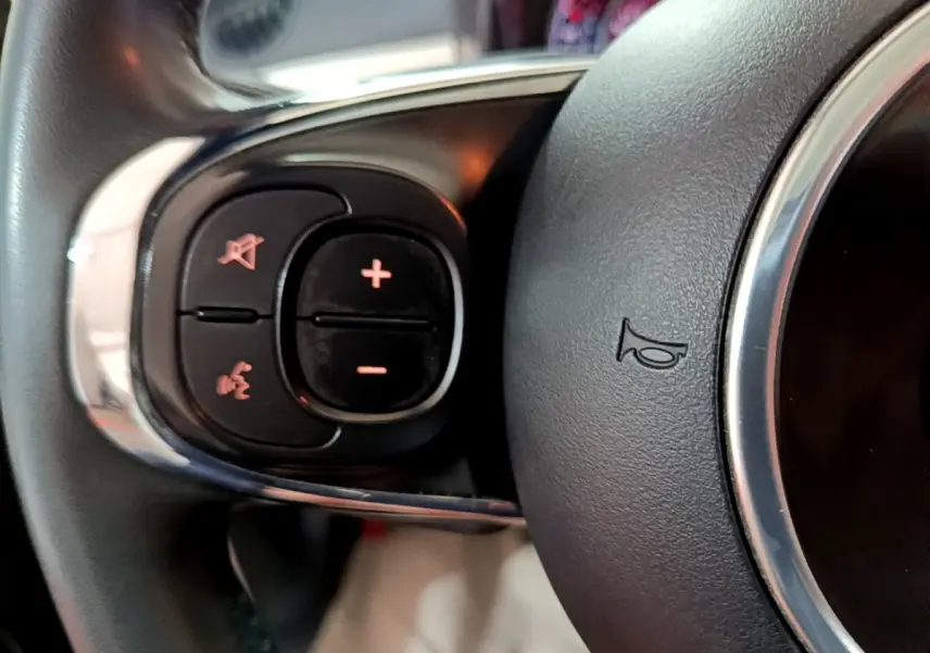Gros plan sur les commandes gauche du volant cuir de la Fiat 500 blanche Hybrid 2021, avec boutons de volume et téléphone.