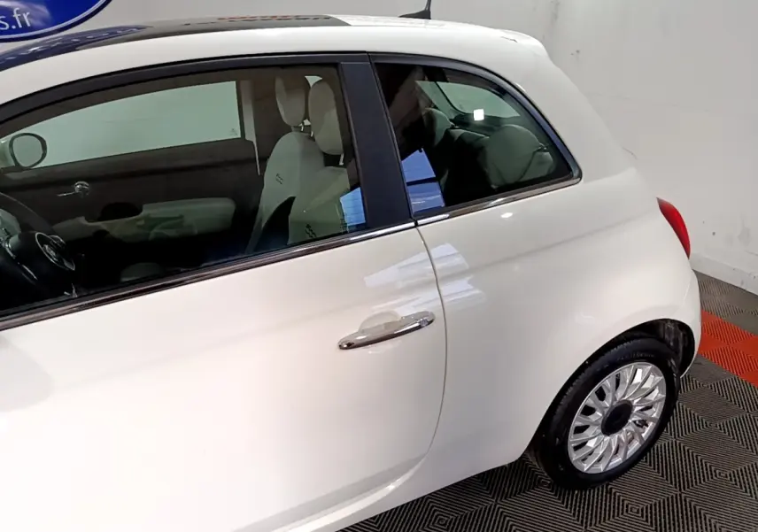 Vue latérale droite d'une Fiat 500 blanche avec jantes argentées et intérieur clair visible.