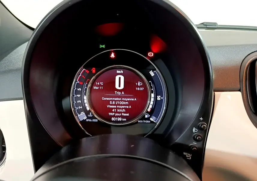 Vue rapprochée du tableau de bord numérique circulaire de la Fiat 500 blanche, affichant la consommation et la vitesse.