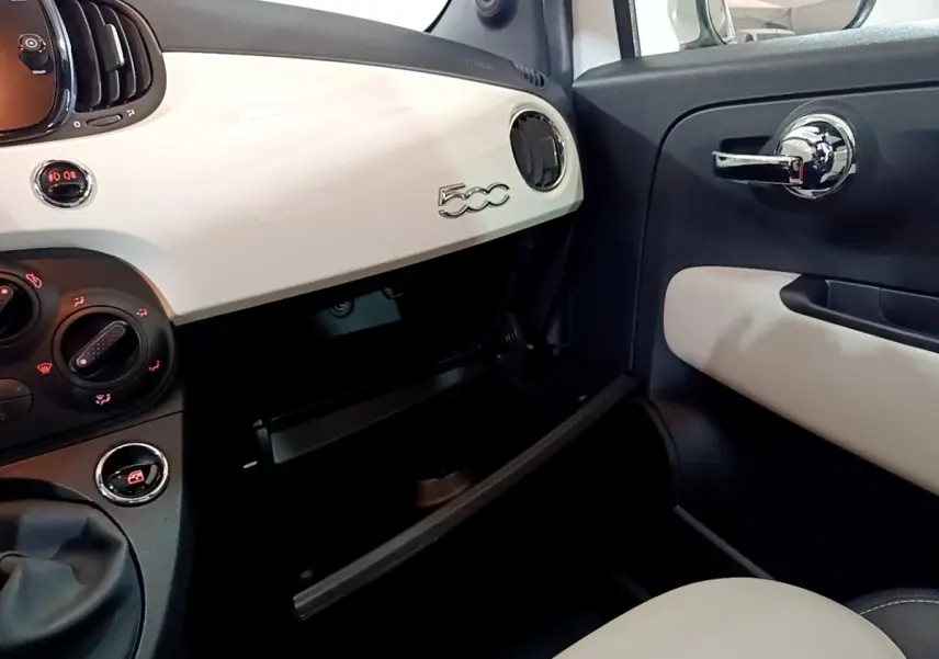 Vue intérieure côté passager de la FIAT 500 blanche, tableau de bord avec logo 500 et boîte à gants ouverte.