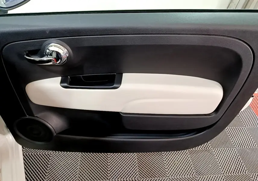 Vue intérieure du panneau de porte côté conducteur de la FIAT 500 blanc avec poignée chromée et insert beige.