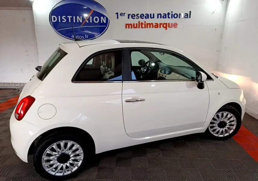 Profil droit d'une FIAT 500 blanche hybride 2021 stationnée en intérieur avec jantes argentées et toit blanc.