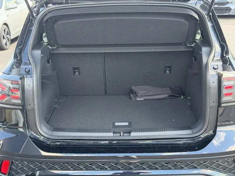Coffre ouvert vu de l'arrière d'un Volkswagen T-Cross noir intense nacré avec intérieur de coffre gris et sac noir posé.