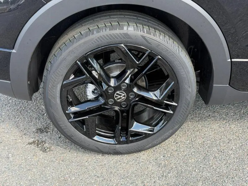 Gros plan sur la roue avant droite du Volkswagen T-Cross noir intense nacré avec jante alu noire brillante R-Line.