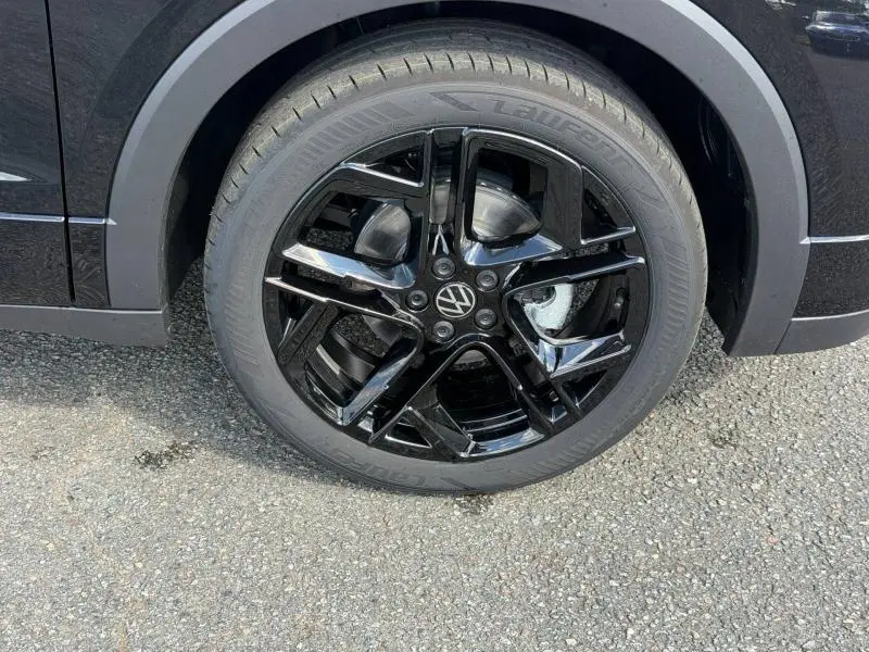 Gros plan sur la jante noire brillante d’un Volkswagen T-Cross noir intense nacré, avec logo VW au centre.