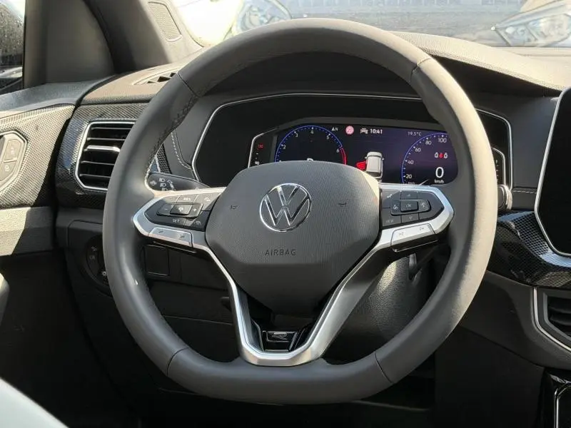 Vue rapprochée du volant cuir multifonction noir du Volkswagen T-Cross 2026 avec tableau de bord numérique en arrière-plan.